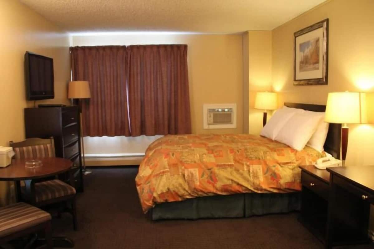 Habitación de hotel con cama, escritorio, silla, una mesita, televisión, ventana con cortinas y un cuadro en la pared.