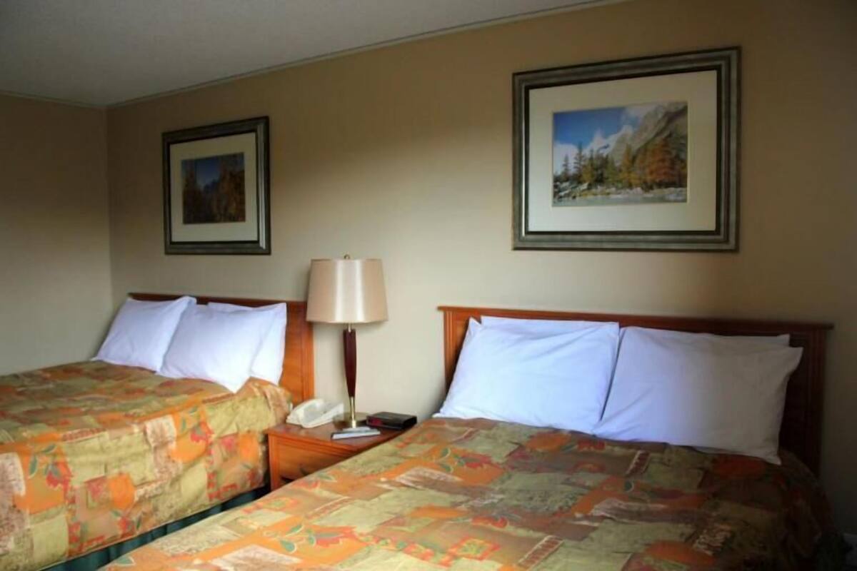 Habitación de hotel con dos camas, una mesita de noche, una lámpara y cuadros en las paredes.