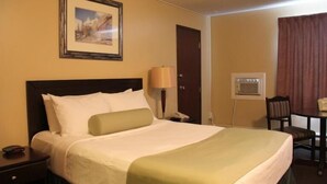 Une chambre d’hôtel comprenant un lit, une table de chevet, une lampe, un bureau, une chaise et un tableau encadré au mur.
