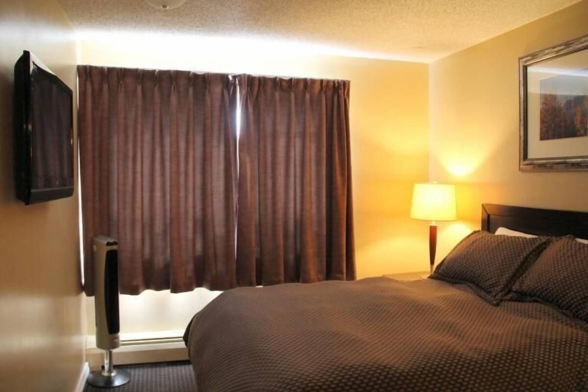 Habitación de hotel con cama, cortinas, lámpara y televisión en la pared.
