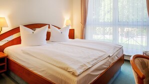 Una cama bien hecha con sábanas blancas y dos almohadas, un cabecero de madera y una mesita de noche con una lámpara.