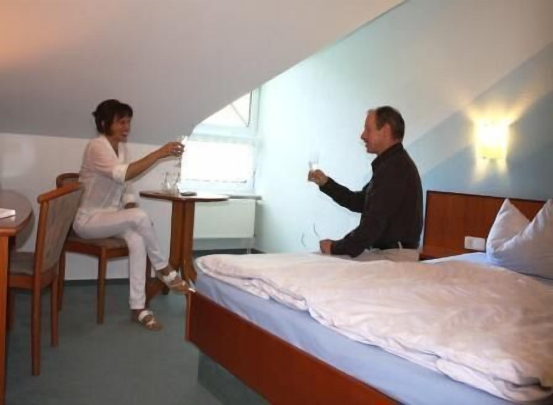 A hotel room with a bed, a small table, and two people sitting at the table.