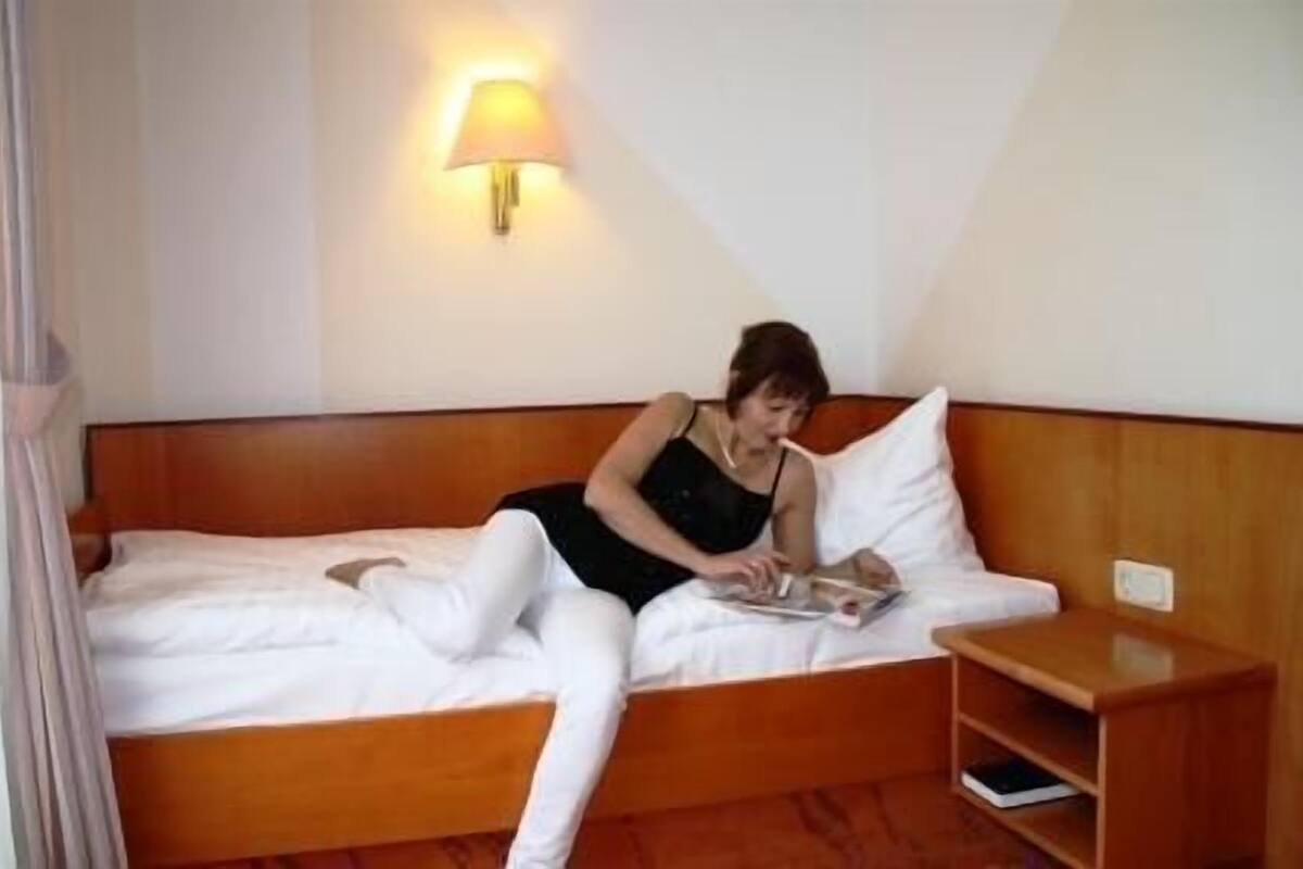 A bed with a wooden headboard, a bedside table, and a wall-mounted lamp.