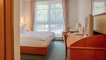 A hotel room with a bed, a desk, a chair, a lamp, a TV, and a window with curtains.
