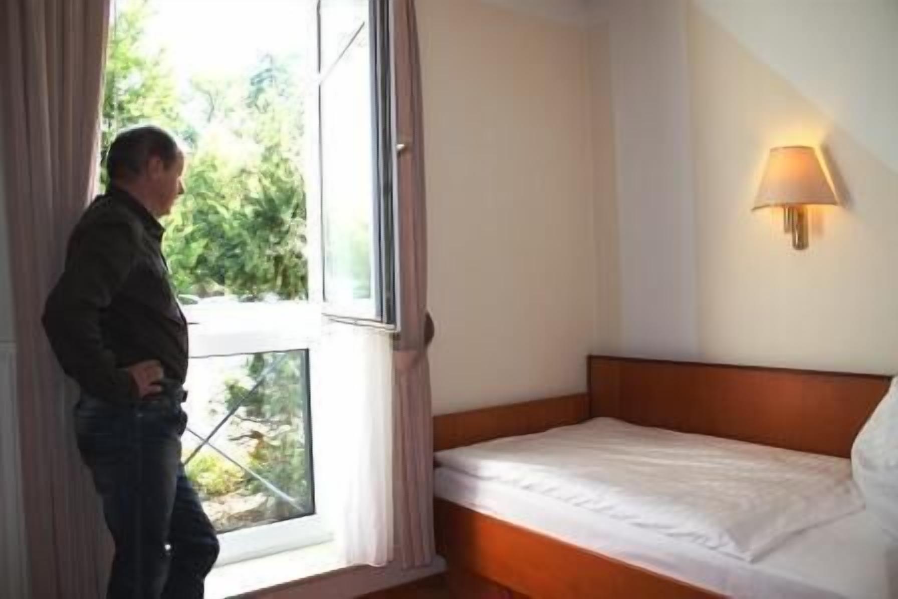 A hotel room with a single bed, a window with curtains, and a wall-mounted lamp.