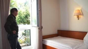 A hotel room with a single bed, a window with curtains, and a wall-mounted lamp.