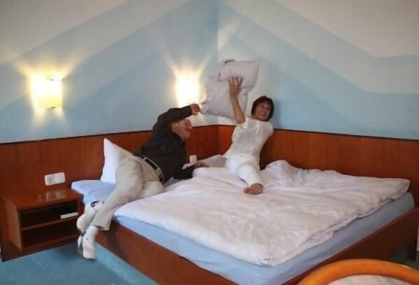 Una cama con sábanas blancas y un cabecero de madera. Junto a la cama, una mesita de noche con una lámpara.