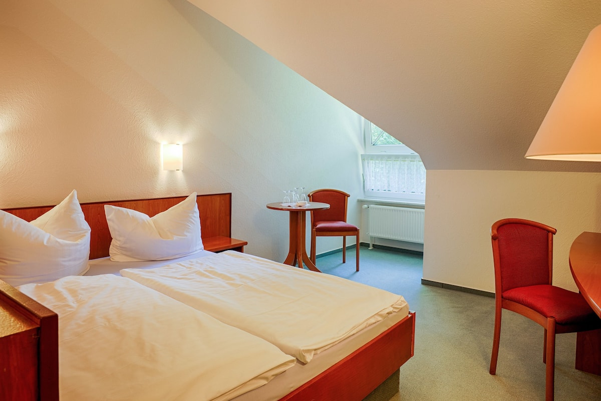 A hotel room with a bed, a small table, a chair, and a lamp.