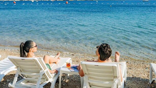 Two people sitting on white chairs facing a body of water with boats in the distance. - Bitez Garden Life Hotel - All Inclusive (Bodrum)