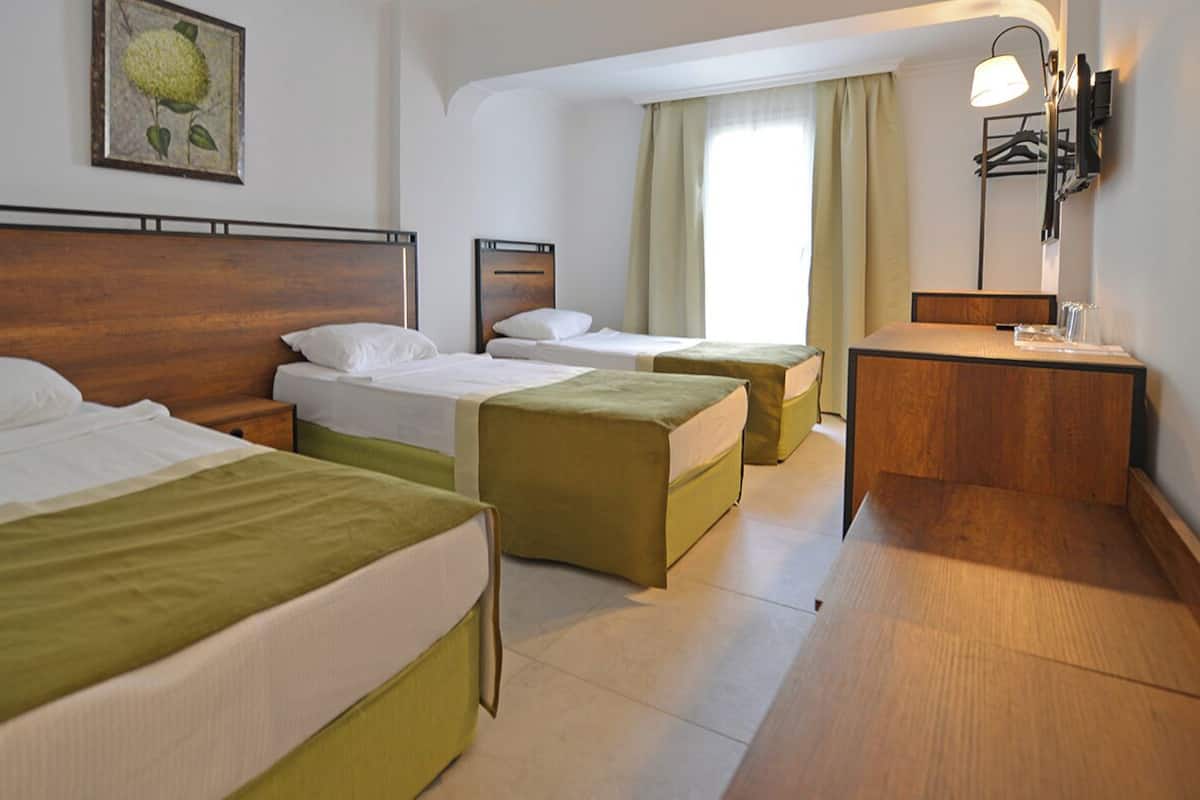 A hotel room with two single beds, a small desk, a mirror, and a window with curtains.