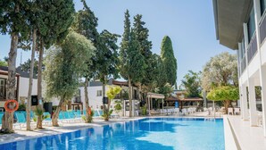 A swimming pool with lounge chairs and umbrellas, surrounded by trees and buildings. - Bitez Garden Life Hotel - All Inclusive (Bodrum)