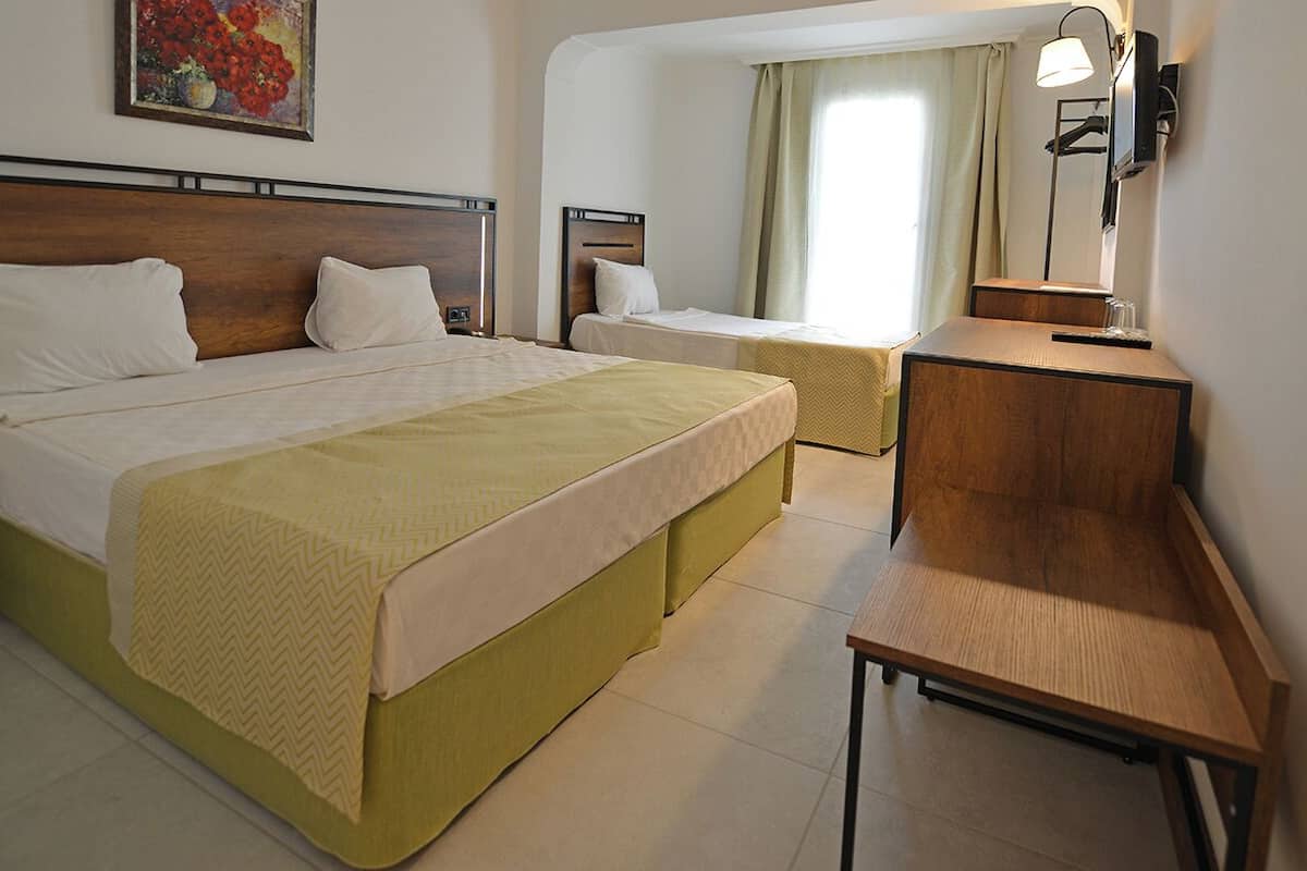 A hotel room with a large bed, a smaller bed, a desk, a chair, a nightstand, a lamp, and a painting on the wall.
