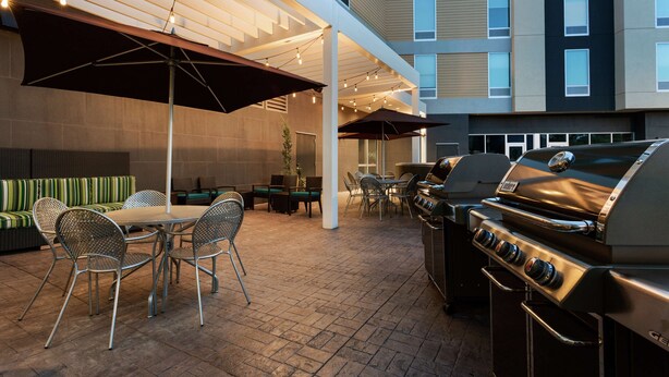 An outdoor patio with a grill, dining area, and umbrellas. - Home2 Suites by Hilton Salt Lake City-Murray, UT (Murray)