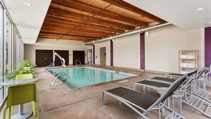 An indoor swimming pool with lounge chairs, a wooden ceiling, and a glass wall. - Home2 Suites by Hilton Salt Lake City-Murray, UT (Murray)