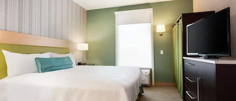 A hotel room with a bed, a television, a nightstand, and a window with curtains.