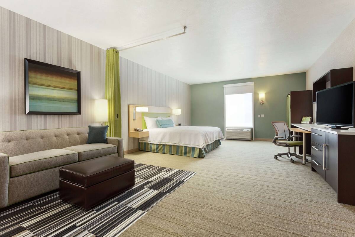 A hotel room with a bed, a sofa, a desk, a television, and a painting on the wall.