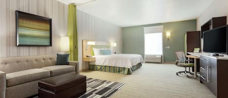A hotel room with a bed, a sofa, a desk, a television, and a painting on the wall.