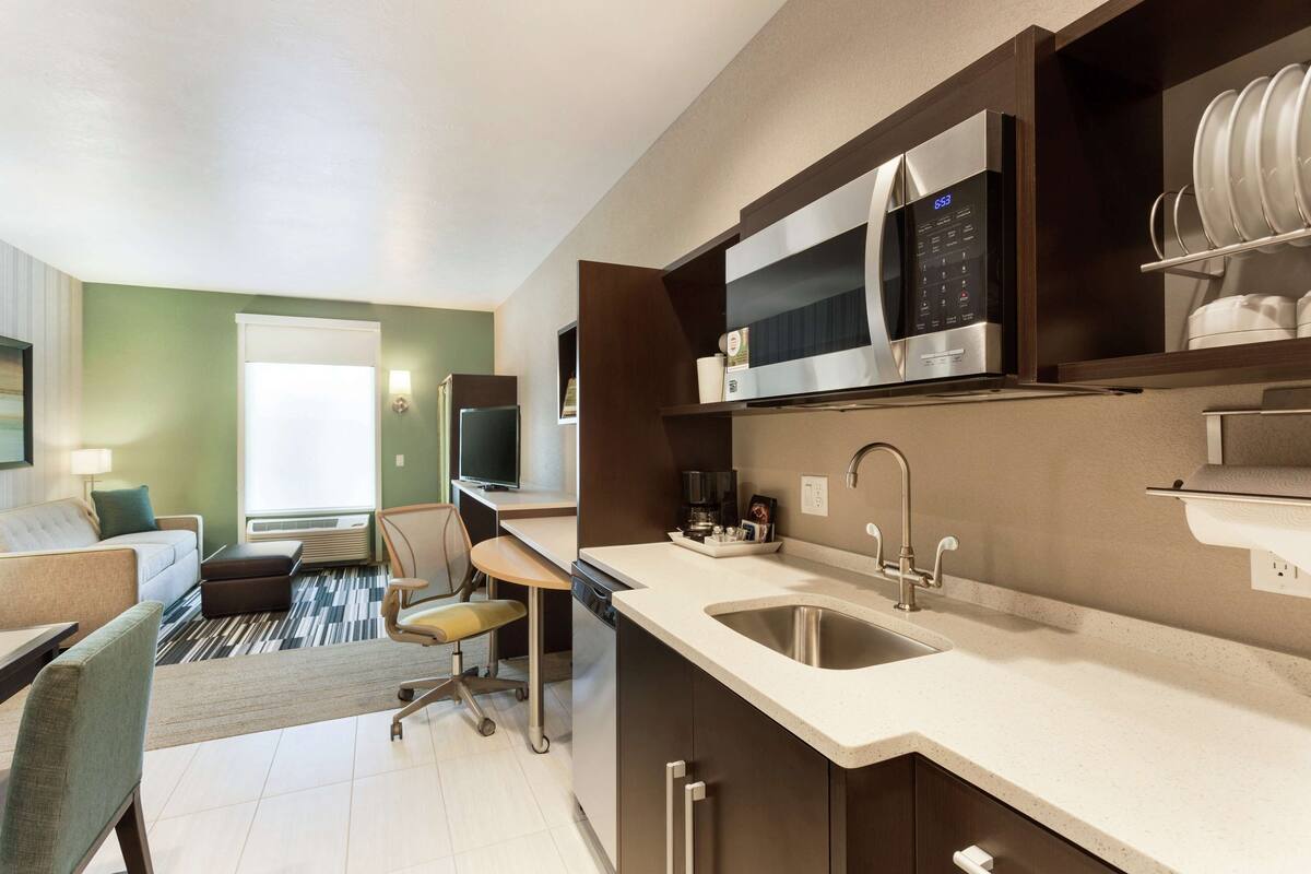 A modern kitchen with a microwave, sink, and a dining area with a sofa and chair.