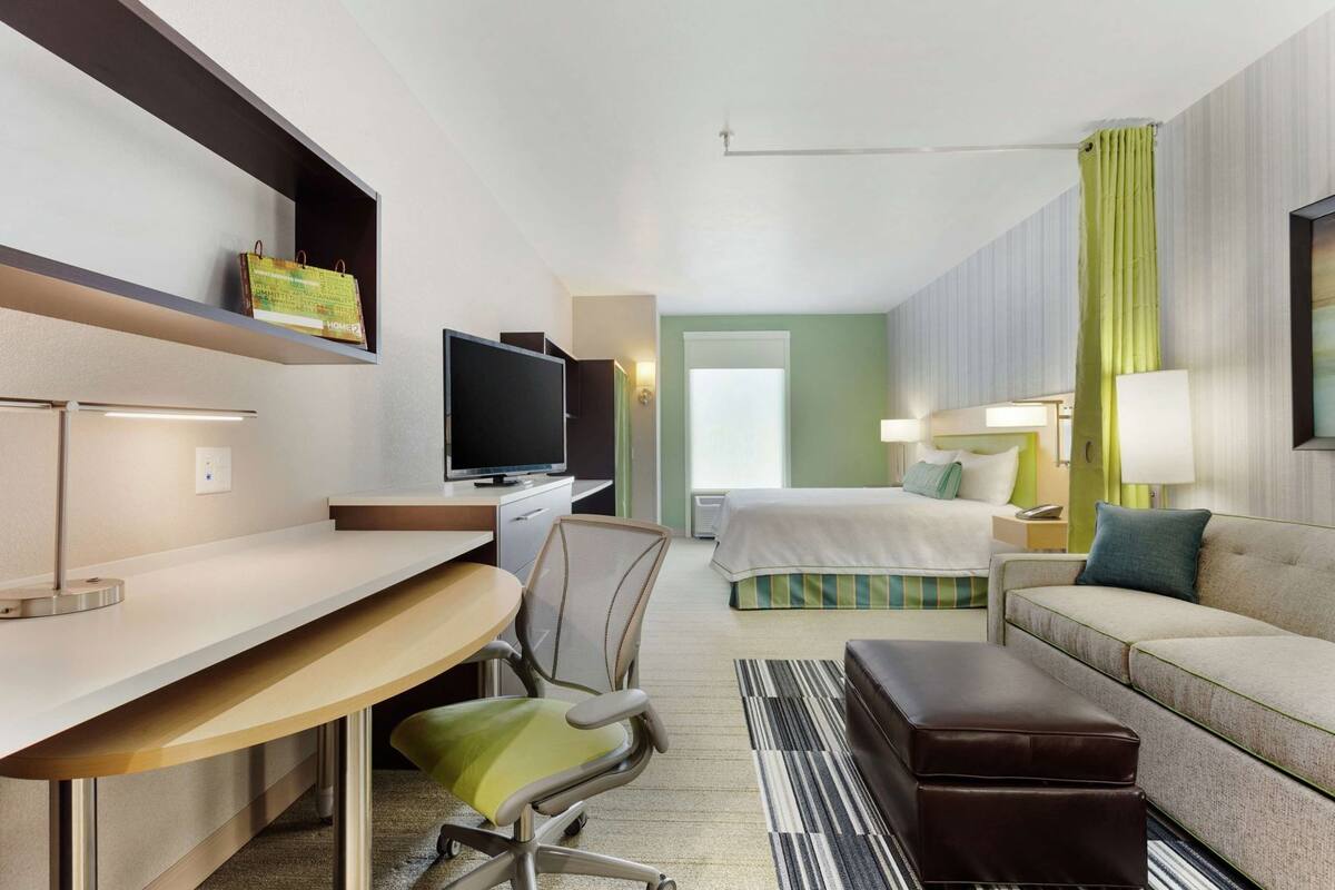 A hotel room with a desk, chair, television, bed, and a sofa.
