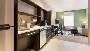 A compact kitchen with a dishwasher, microwave, and a small dining area with a chair and table. - Home2 Suites by Hilton Salt Lake City-Murray, UT (Murray)
