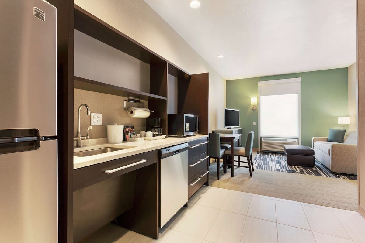 A compact kitchen with a dishwasher, microwave, and a small dining area with a chair and table.