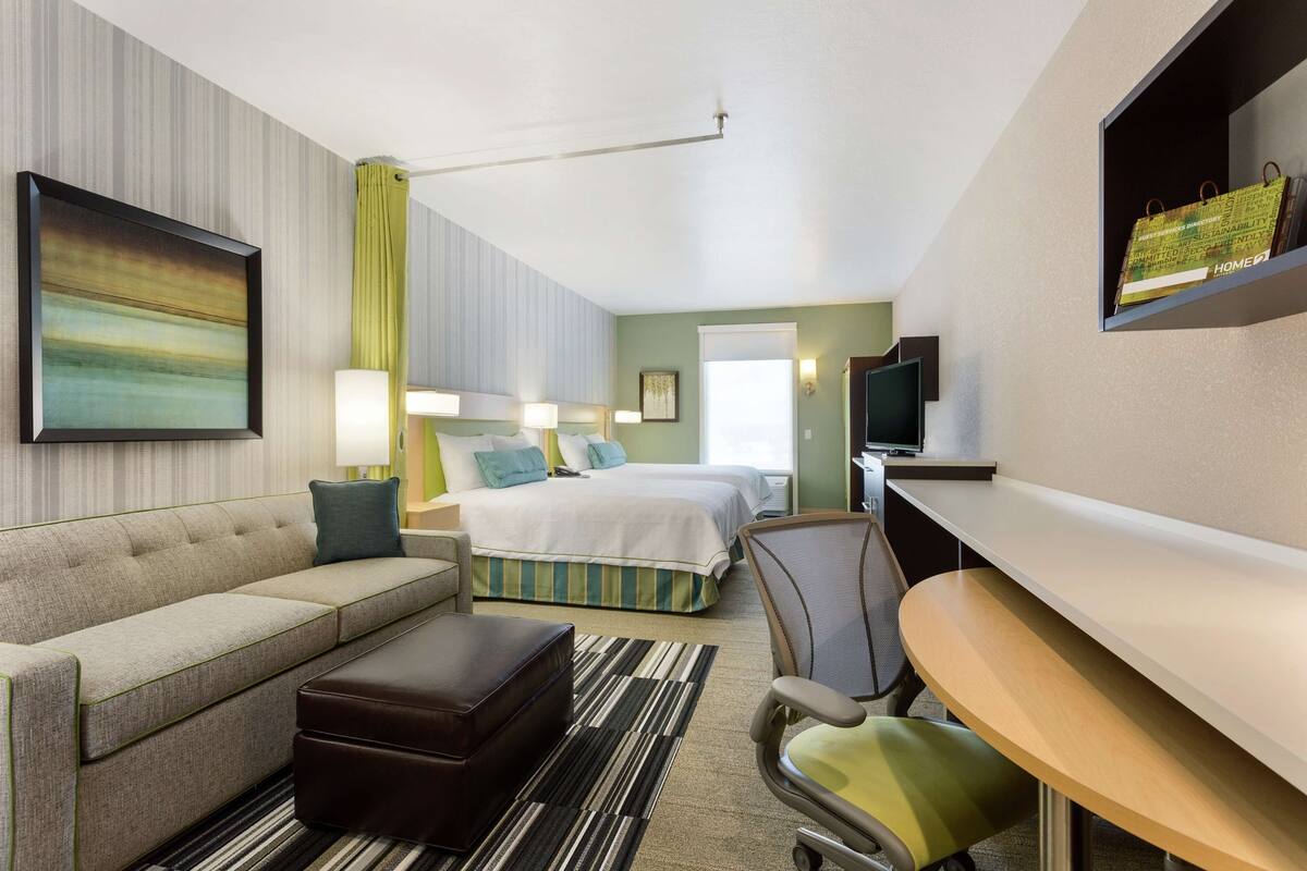 A hotel room with a bed, a sofa, a desk, and a TV.