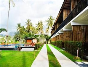 A pathway leading to a building with a modern design, surrounded by lush greenery and palm trees. - The Nidhra (Ko Pha-ngan)