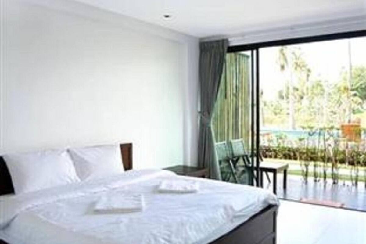 A modern hotel room with a large bed, a balcony with a view of greenery, and a large window.