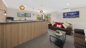 Un hall d’hôtel avec un comptoir d’accueil, un canapé marron agrémenté de coussins rouges et blancs, et une enseigne indiquant « Comfort Inn Serenity Bathurst ».