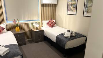 Habitación de hotel con dos camas, una mesita de noche con lámpara, aire acondicionado instalado en la pared y dos cuadros enmarcados.