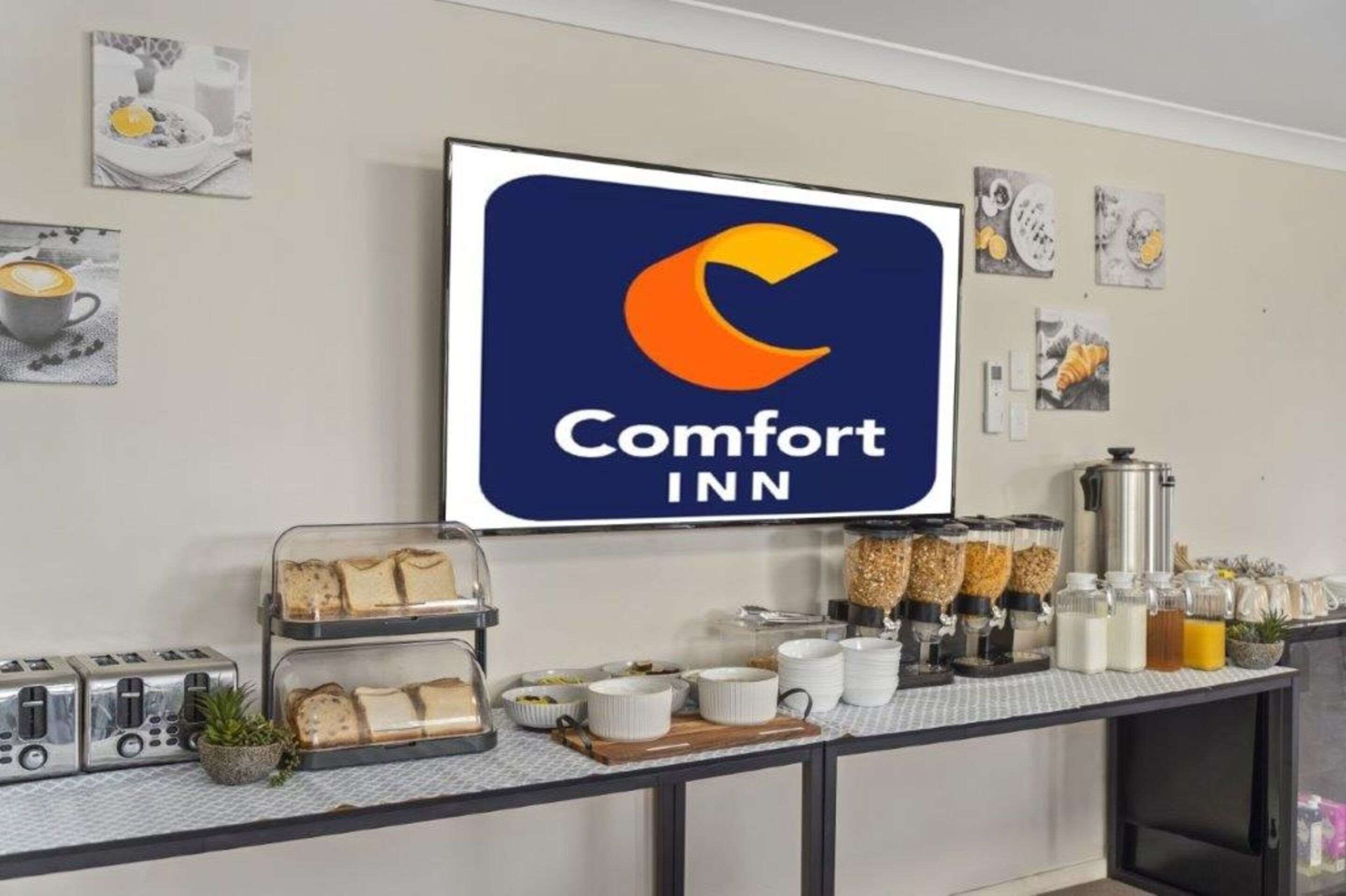 A breakfast buffet area with a Comfort Inn sign, toasters, bread, and various food containers.
