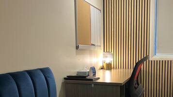 A room with a blue sofa, a wooden desk with a lamp, a chair, and a window.