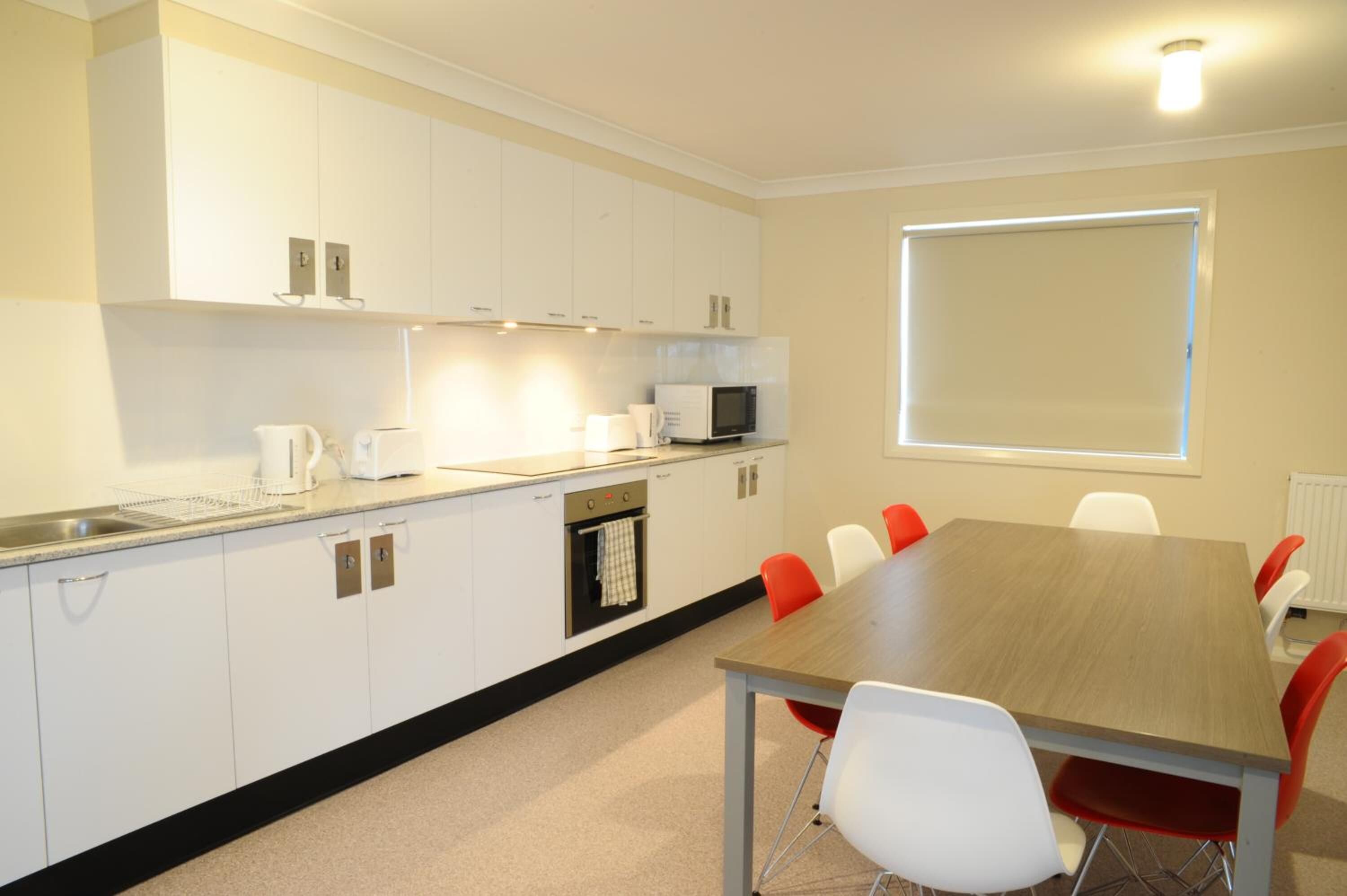 A modern kitchen with white cabinets, a microwave, and a dining table with red chairs.