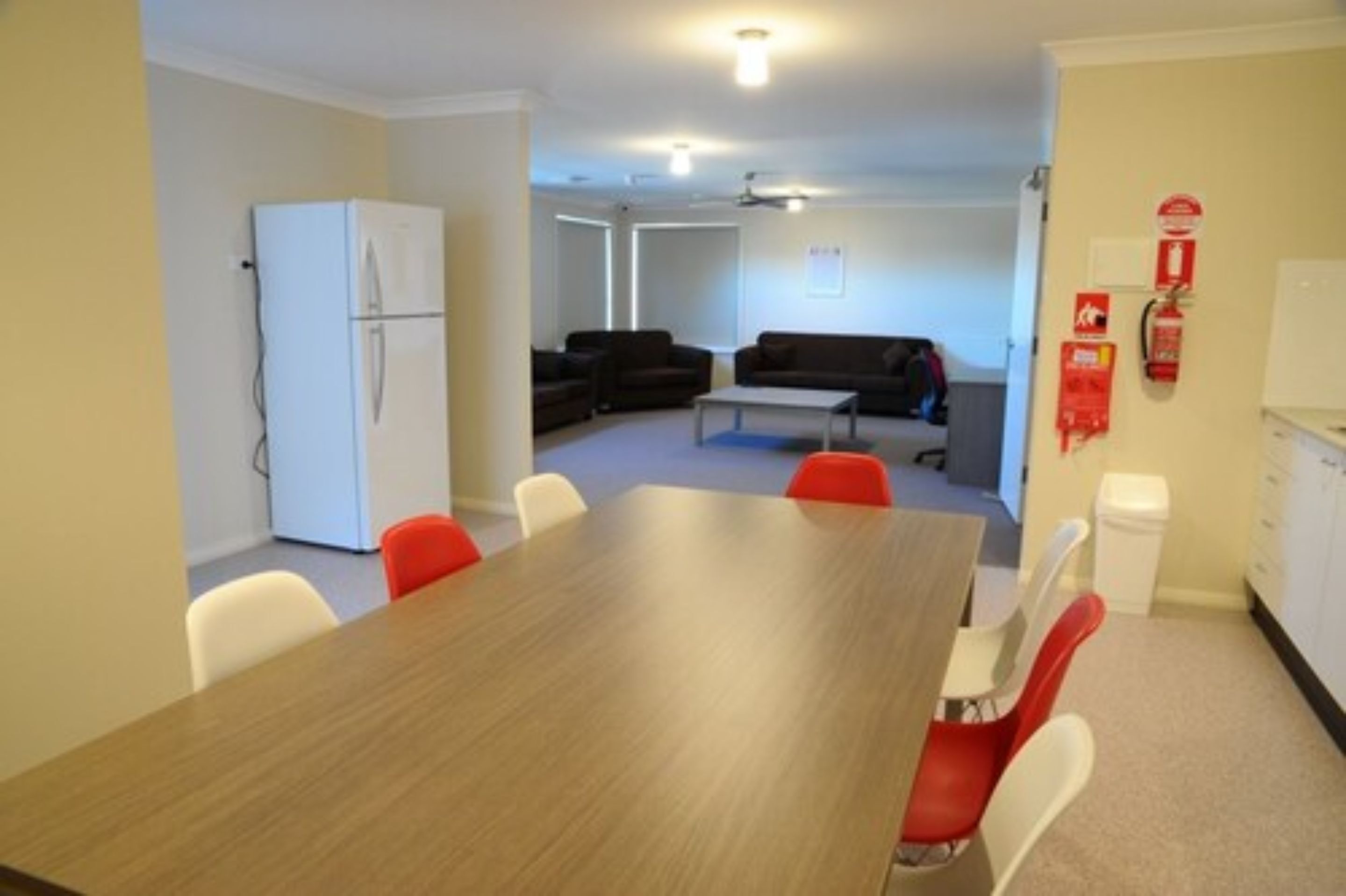 A modern room with a wooden dining table, red and white chairs, a white refrigerator, a black sofa, and a white couch.