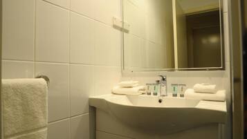 Un baño con lavamanos blanco, espejo y toallero.