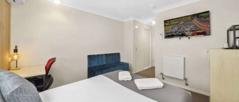 Hotelkamer met een bed, een bureau met stoel, een blauwe fauteuil, een radiator en een tv aan de muur met een racedebuut.