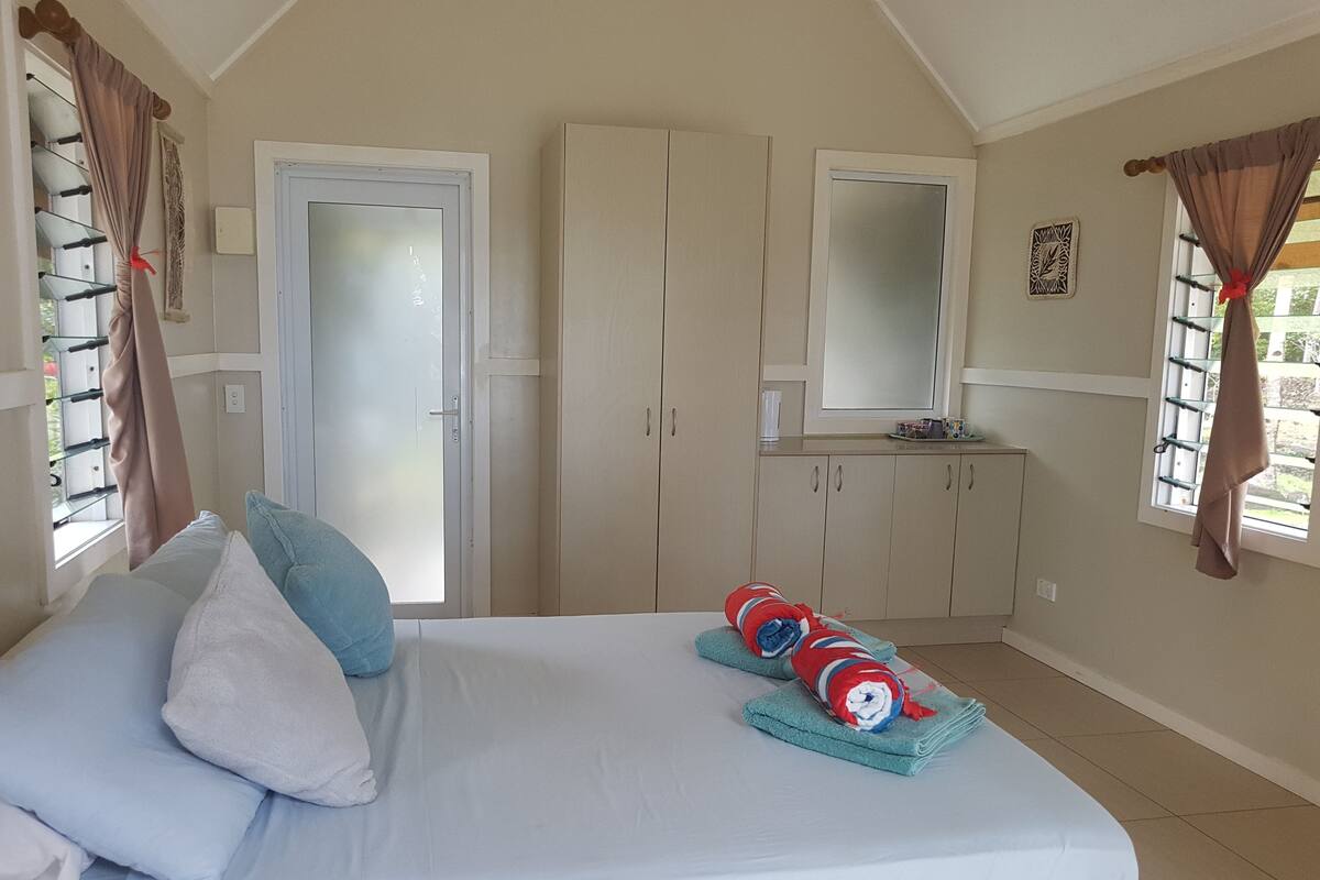 Un dormitorio con cama, almohadas, un armario, un espejo y una ventana con cortinas.