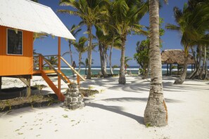 Ein Gebäude am Strand mit einem Reetdach, umgeben von Palmen und einem Sandstrand.