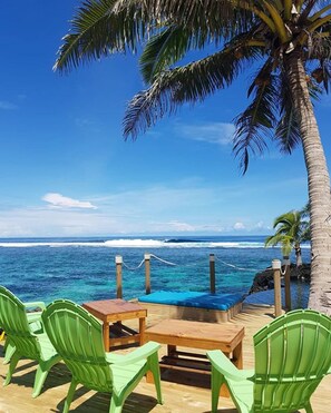 A wooden deck with green chairs and a table overlooking a beach with clear blue water and a palm tree. - Sa'Moana Beach Bungalows (Salamumu)