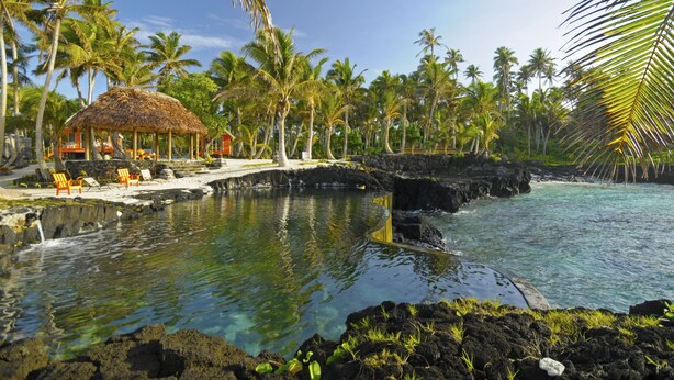 A tropical resort with a thatched-roof hut, lounge chairs, and a clear pool surrounded by palm trees and rocky terrain. - Sa'Moana Beach Bungalows (Salamumu)