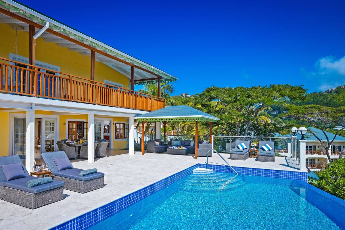 A two-story building with a swimming pool, outdoor seating, and a view of the surrounding landscape.