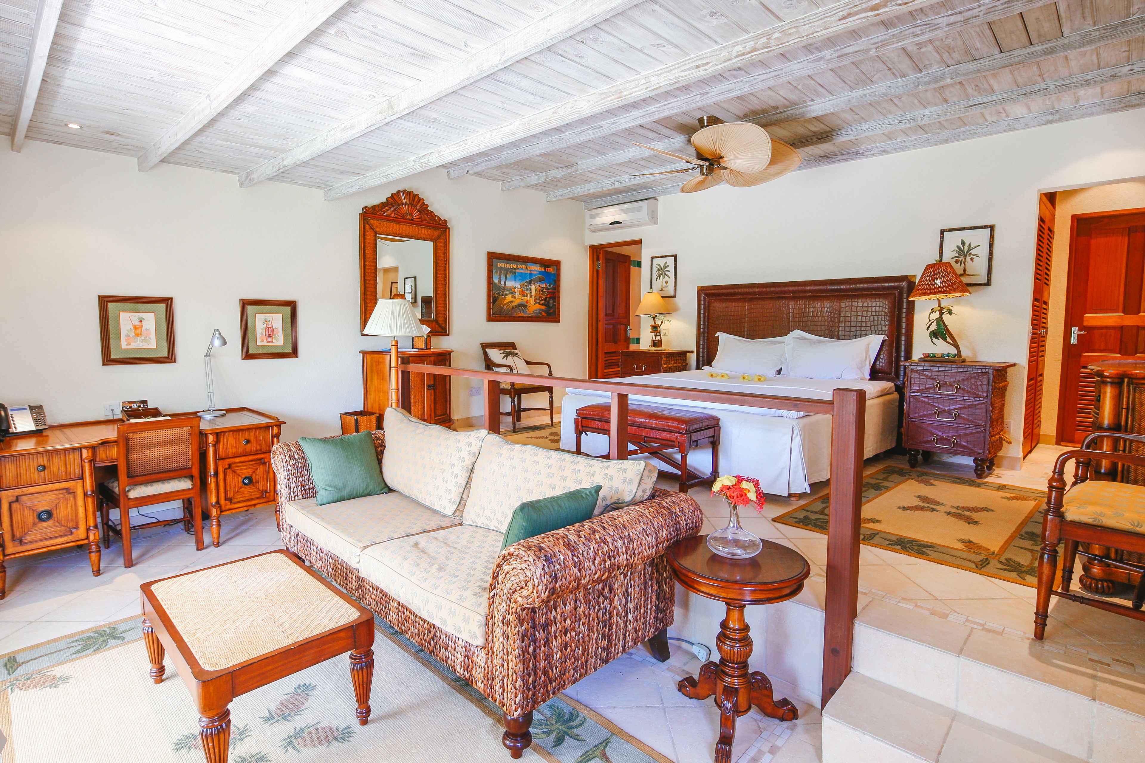 A well-furnished room with a wooden ceiling, a bed with a headboard, a sofa, a desk, and a chair.