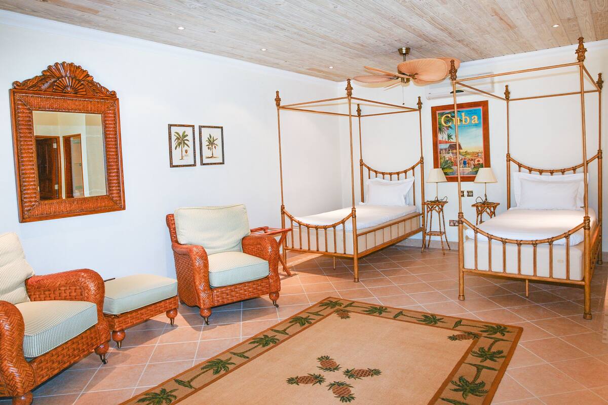 A four-poster bed, two wicker chairs, a mirror, and a framed picture of Cuba.