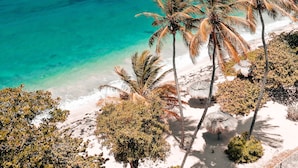 Une plage bordée d’une eau turquoise et limpide, de palmiers et d’îles rocheuses qui se dessinent à l’horizon.