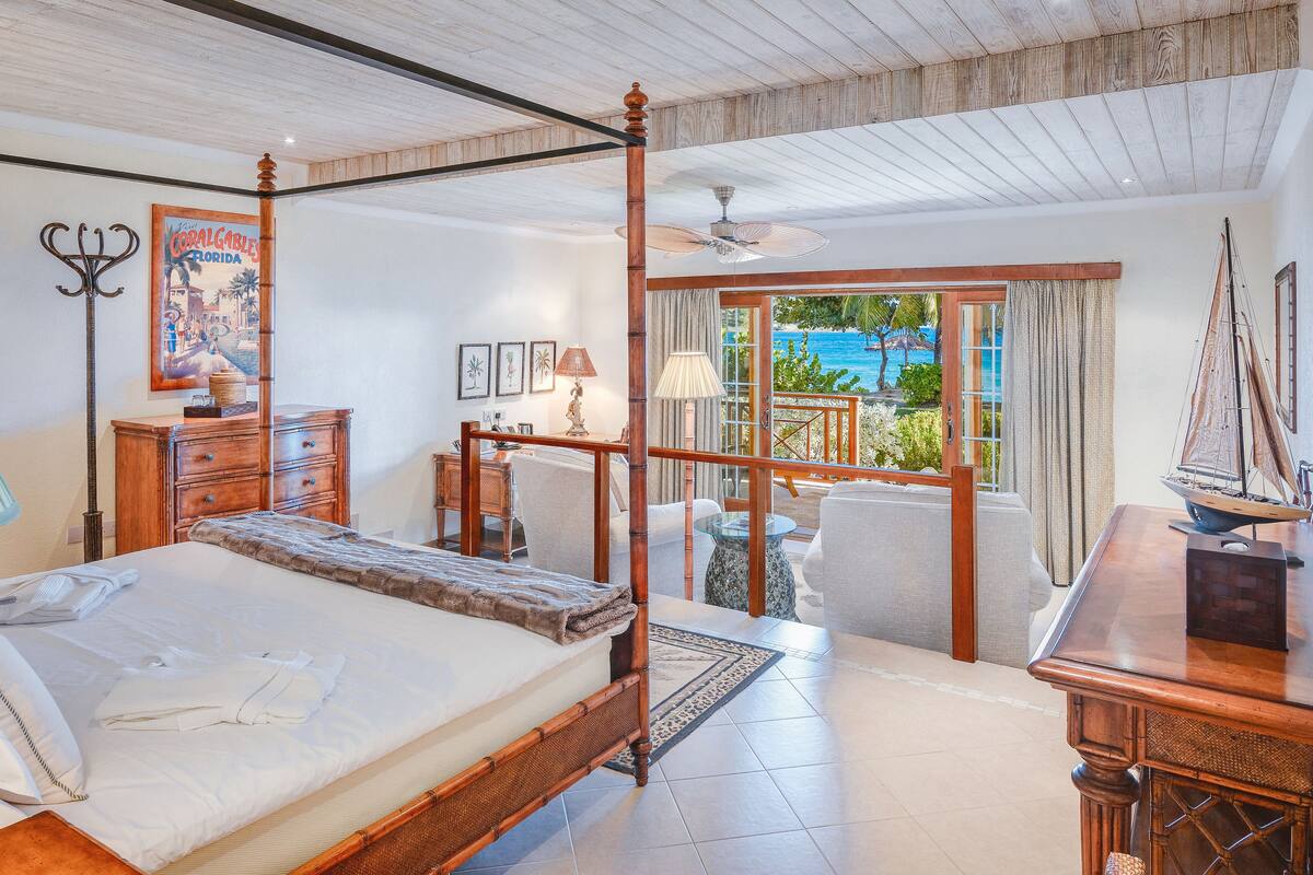 A spacious bedroom with a large bed, a wooden desk, and a balcony with a view of the sea.