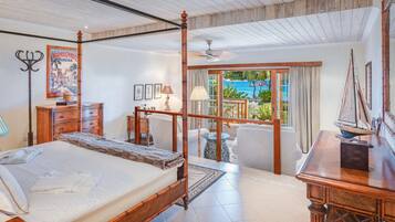 A spacious bedroom with a large bed, a wooden desk, and a balcony with a view of the sea.