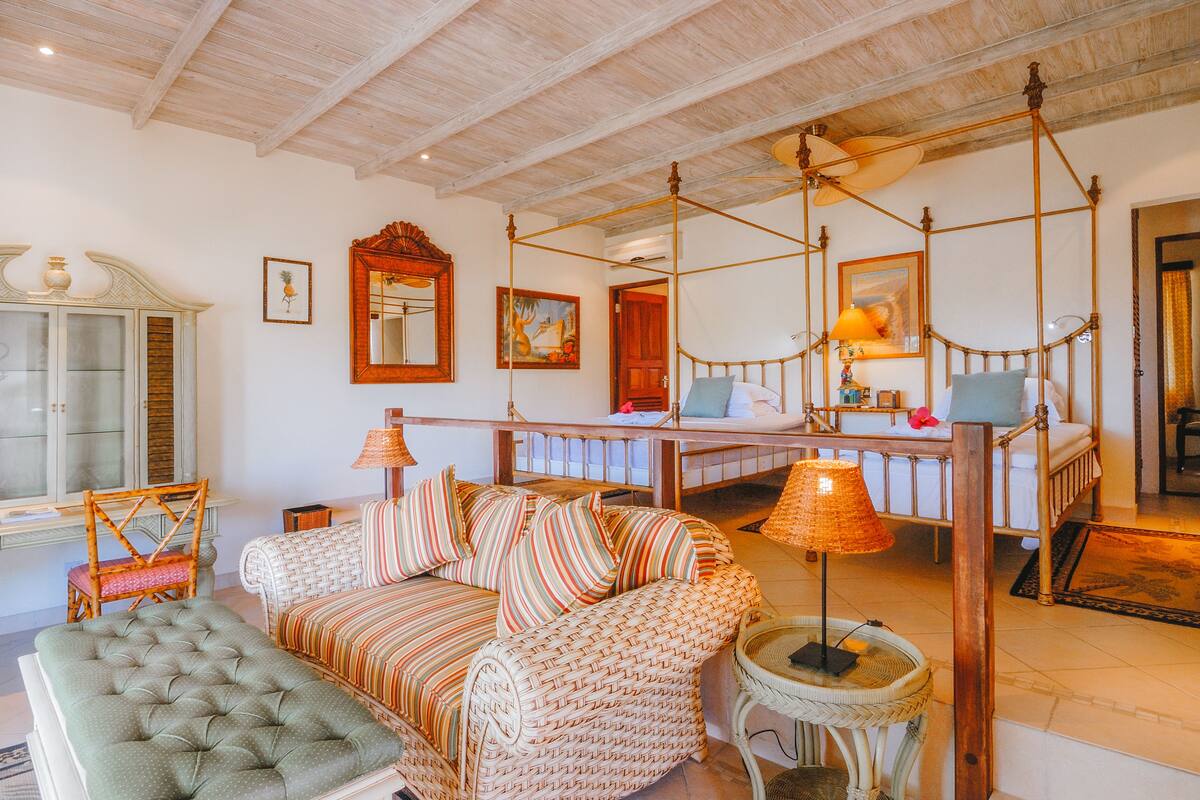 A spacious room with a four-poster bed, a cushioned bench, and a wicker sofa.