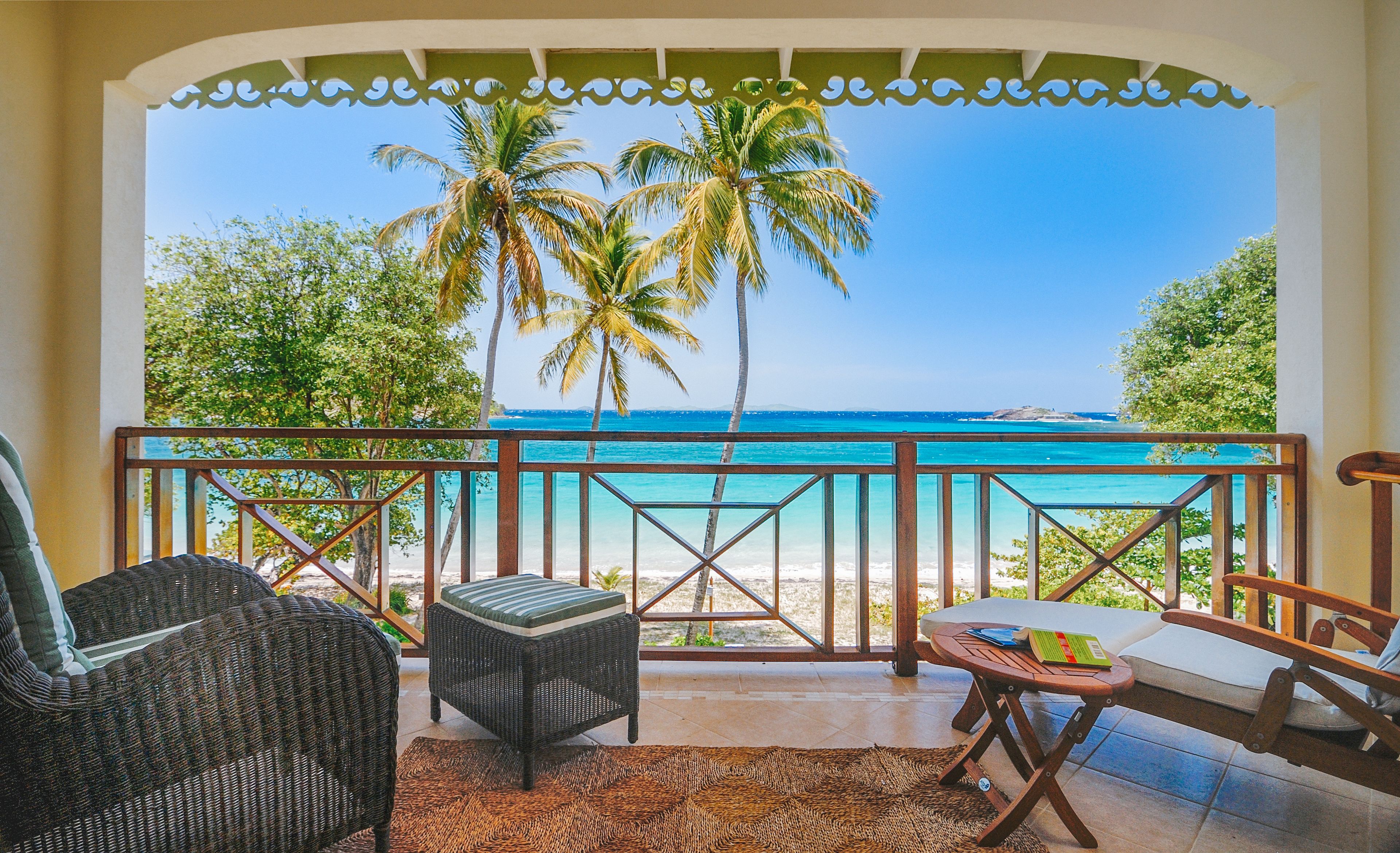 A balcony with wicker furniture, a view of the ocean, and a tropical setting.
