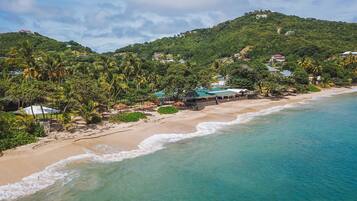 A beach with clear turquoise waters, a sandy shore, and a backdrop of lush green hills with scattered buildings.