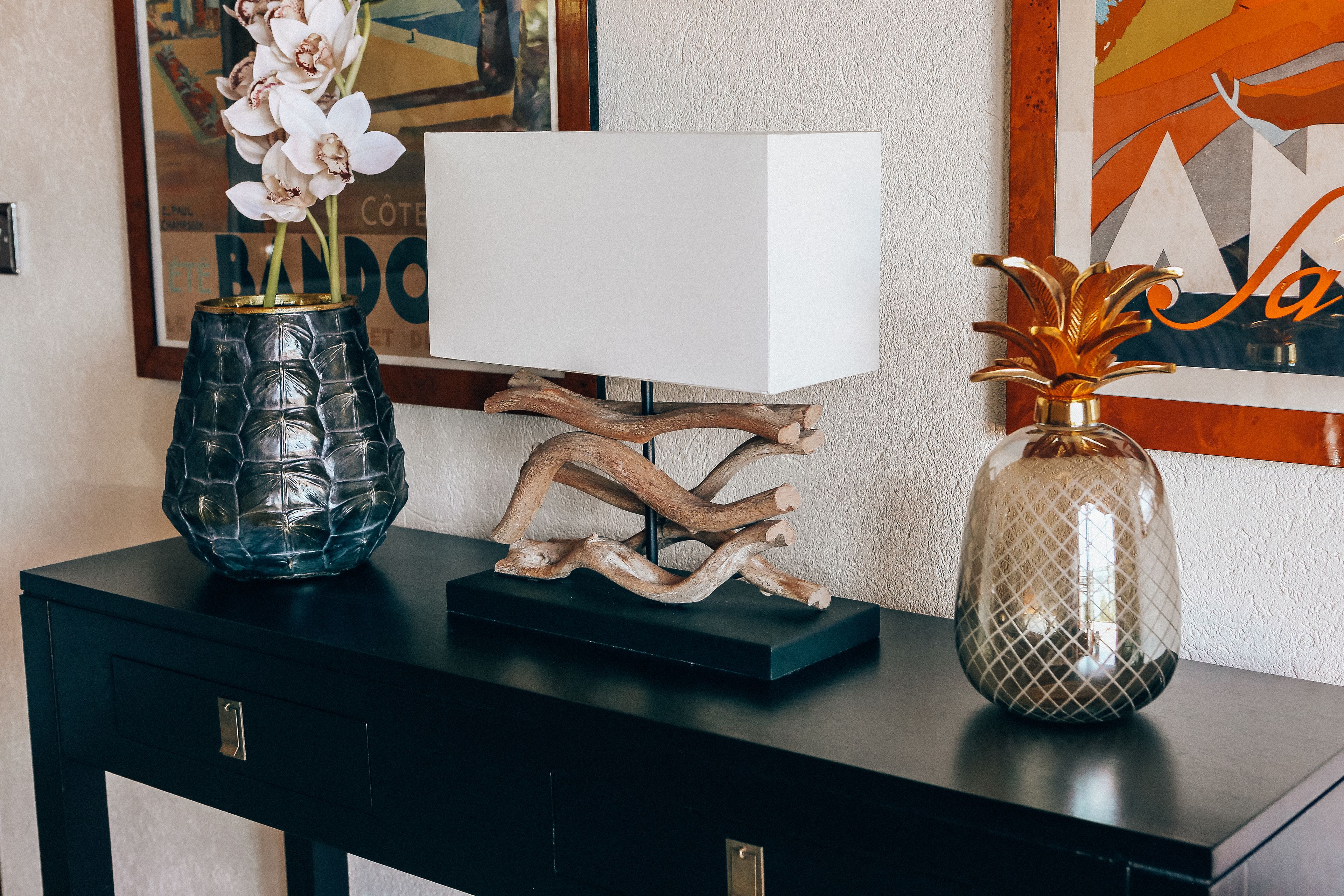 Ein schwarzes Konsolentisch mit einer Glasvase mit Orchideen, einer weißen Lampe und einer Glasvase mit goldener Verzierung.